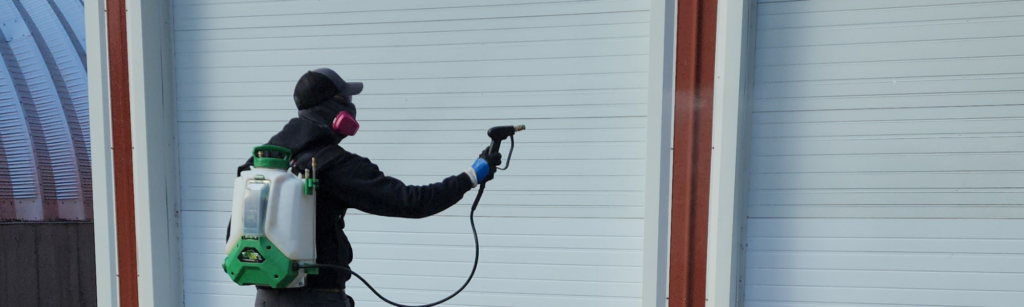 BC technician using an electric backpack sprayer on a large shed